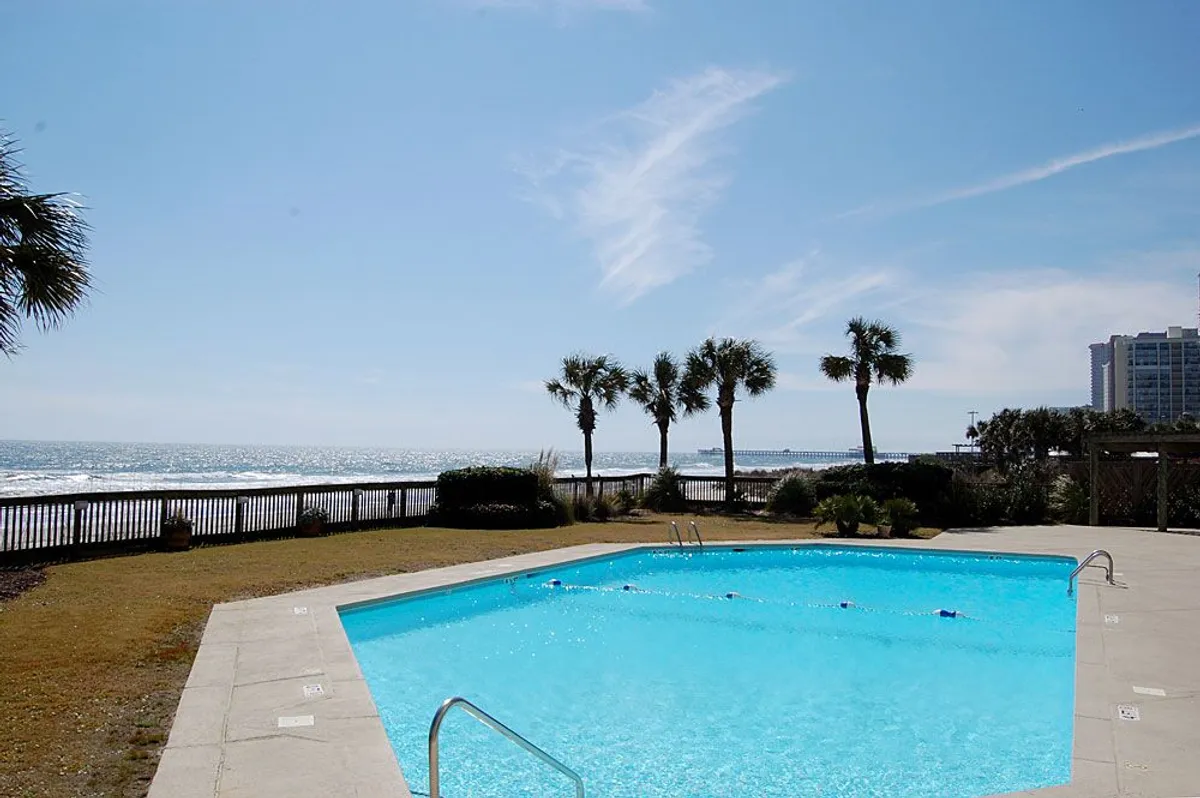 A sparkling swimming pool with lounge chairs and palm trees, set just steps from the ocean. The scene conveys a tranquil, resort-style atmosphere, showcasing where guests can swim, sunbathe, or relax poolside with the ocean visible beyond.