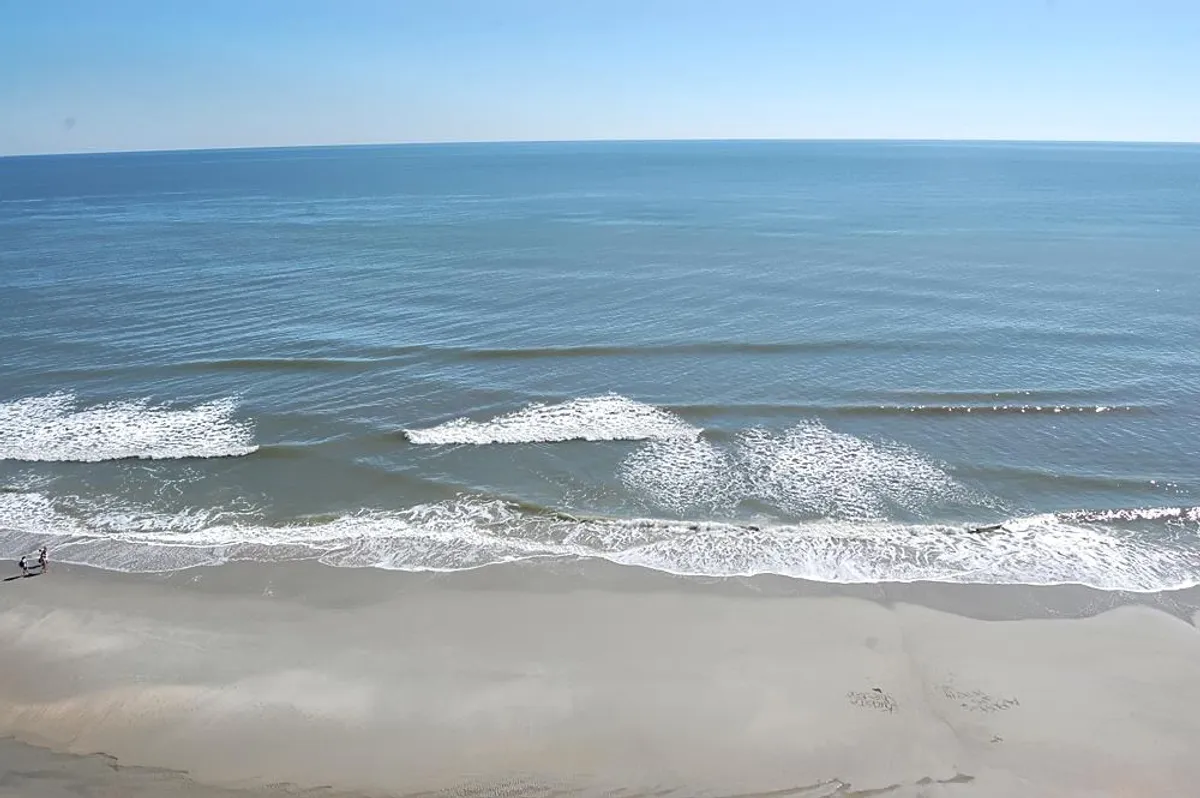 A peaceful shoreline scene showing gentle ocean waves rolling onto a sandy, uncrowded beach. The distant horizon and subtle sunrise hues evoke an atmosphere of serenity and endless possibility for intimate strolls.