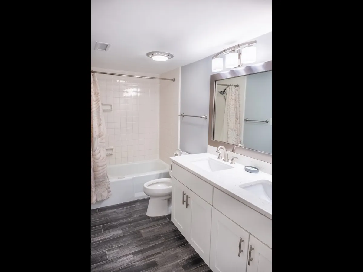 A modern bathroom with a double vanity, stylish light fixtures, a large mirror, and a bathtub. The room is bright, spacious, and designed for both relaxation and convenience.