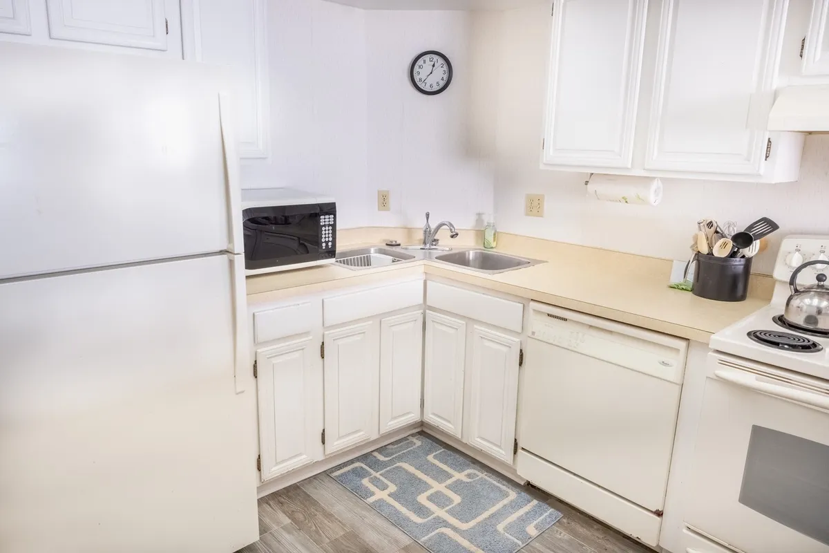 This image shows a warm, welcoming kitchen space with all the essentials clearly visible, including a refrigerator, microwave, sink, dishwasher, and stove. The scene captures a moment of meal preparation, with hints of baking and the possibility of a bustling, social environment. The kitchen looks fully equipped and ready for both everyday and special meals.