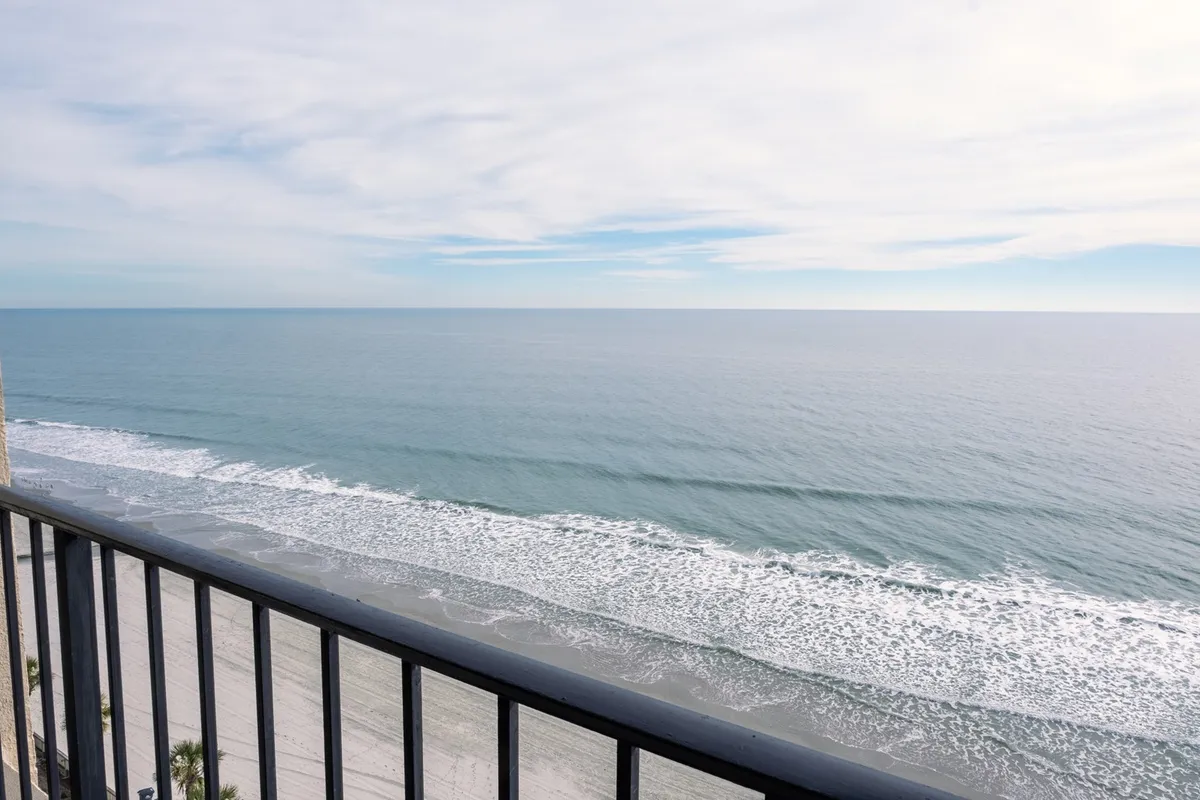 A serene ocean view from a private balcony, featuring gentle waves, a wide expanse of sky, and a balcony railing in the foreground. The tranquil scene evokes a sense of peaceful seclusion, perfect for starting the day or unwinding as a couple.