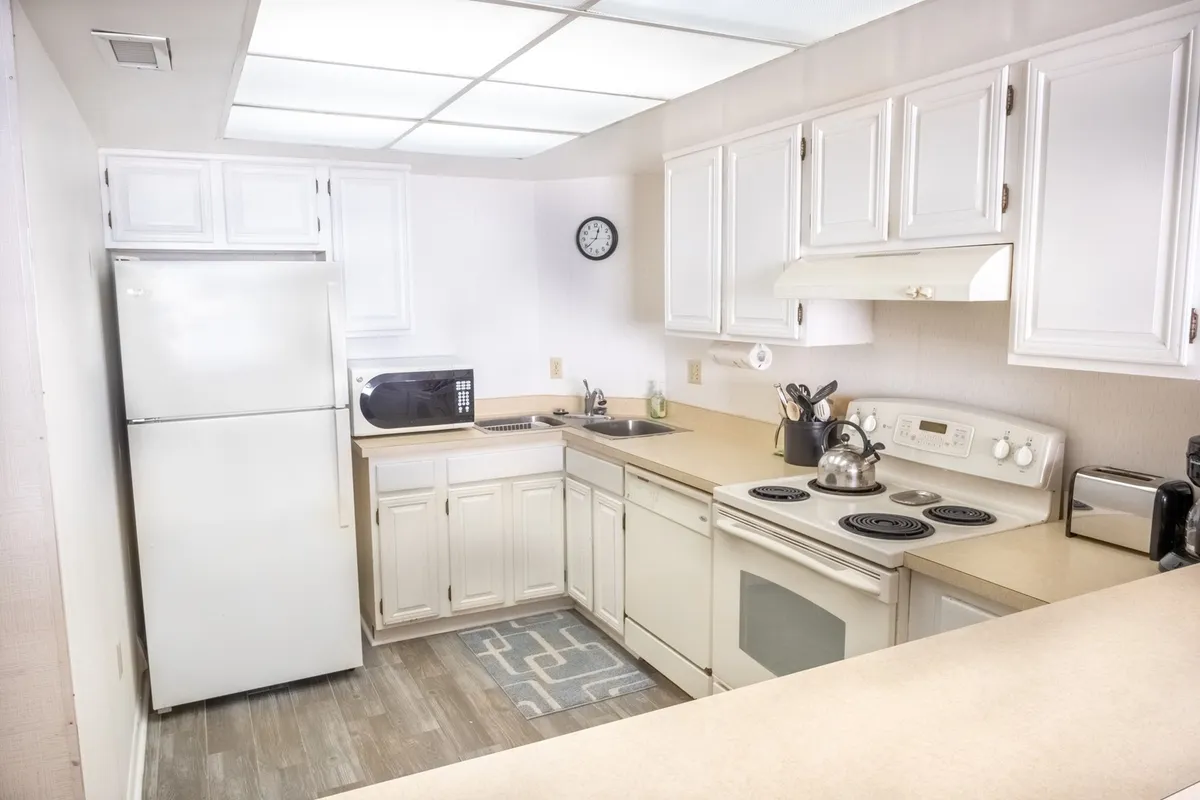 A bright kitchen with white cabinetry, a spacious kitchen island, and sleek stainless steel appliances is featured. The layout suggests ample space for cooking, gathering, and sharing meals. The mood feels both practical and inviting, ideal for preparing family recipes or hosting casual get-togethers.