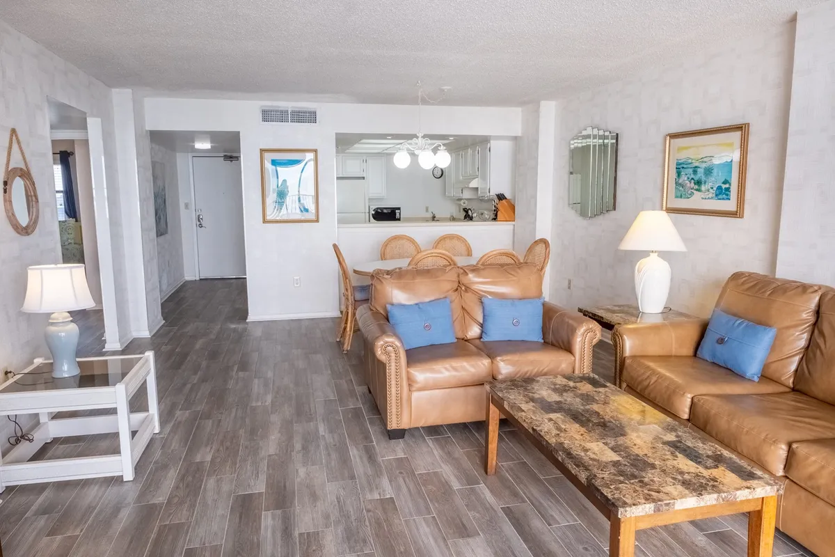 A cozy living room with plush leather sofas, a central coffee table, and framed artwork, creating an inviting atmosphere for family gatherings or unwinding after a day at the beach. The setup encourages conversation and shared moments.